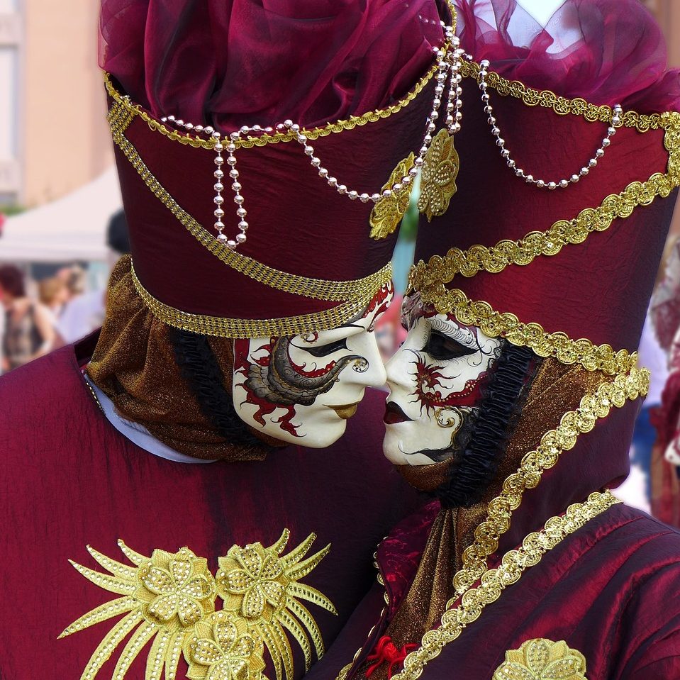 Venedig, venezianische Masken Zwei Menschen mit venezianischen Masken und in festlicher, roter Kleidung mit goldenen Verzierungen, die sich einen Kuss geben möchten.