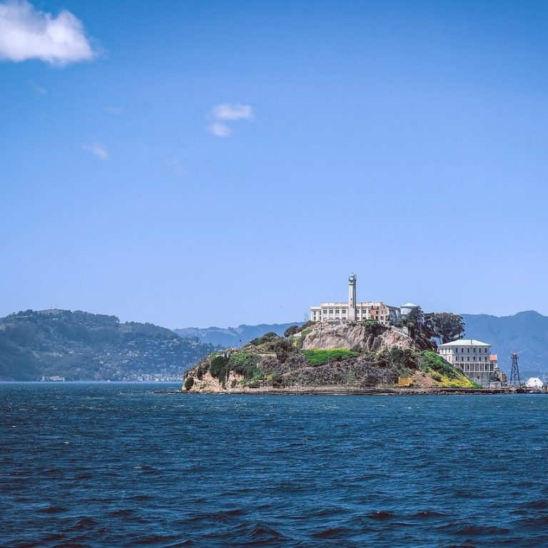 Alcatraz Alcatraz-Insel mit historischen Gebäuden, umgeben von Wasser und Bergen im Hintergrund.