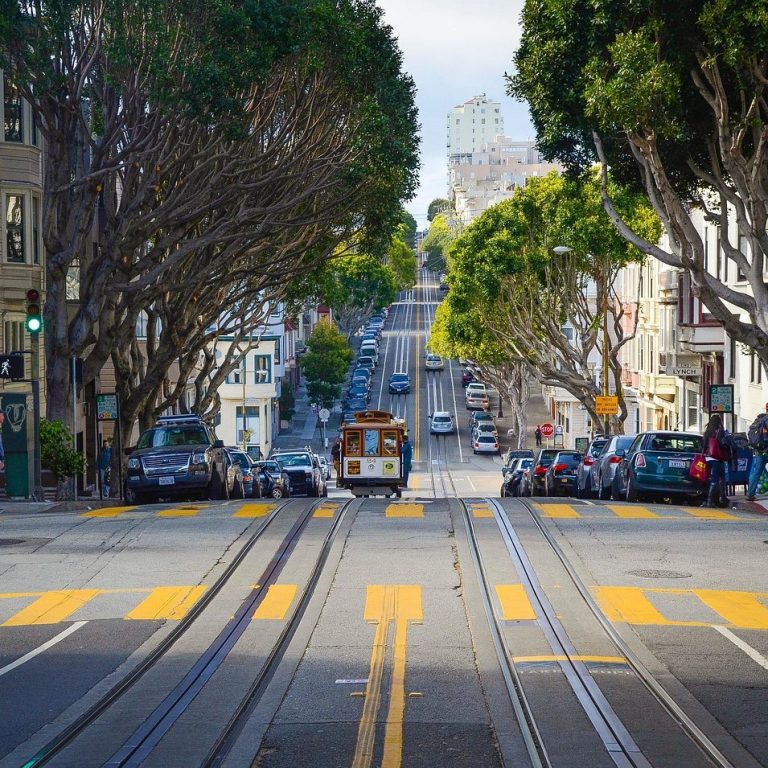 San Francisco Eine steile Straße in San Francisco mit einer Straßenbahn und Bäumen auf beiden Seiten.