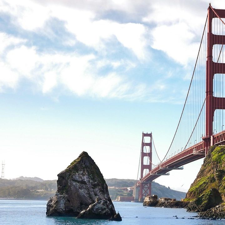 Golden Gate Bridge Rote Golden Gate Bridge, umgeben von Wasser und Felsen, unter einem bewölkten Himmel.